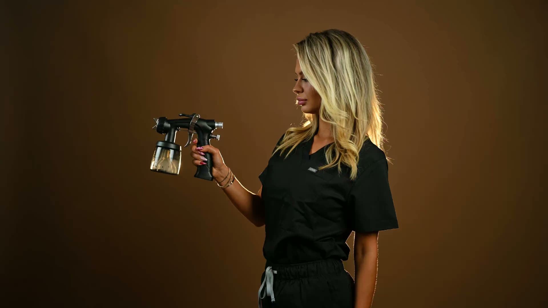Taylor, Sunkiss Studios founder and lead artist, raising her spray tan airbrush in profile against a warm amber backdrop